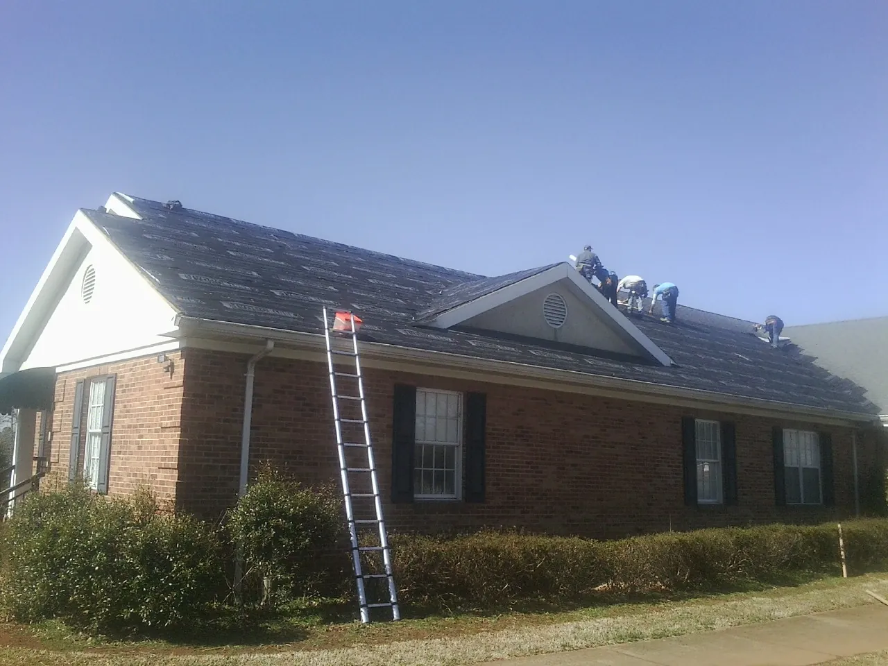 Crew tearing shingles off a brick ranch roof with a ladder set — Emergency Roof Repair work by our crew in Island Heights