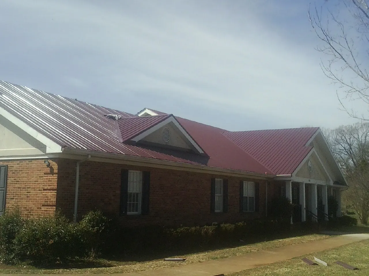 Red metal roof with gabled entries on a long brick building, from a Hail Damage Roof Repair job in Island Heights