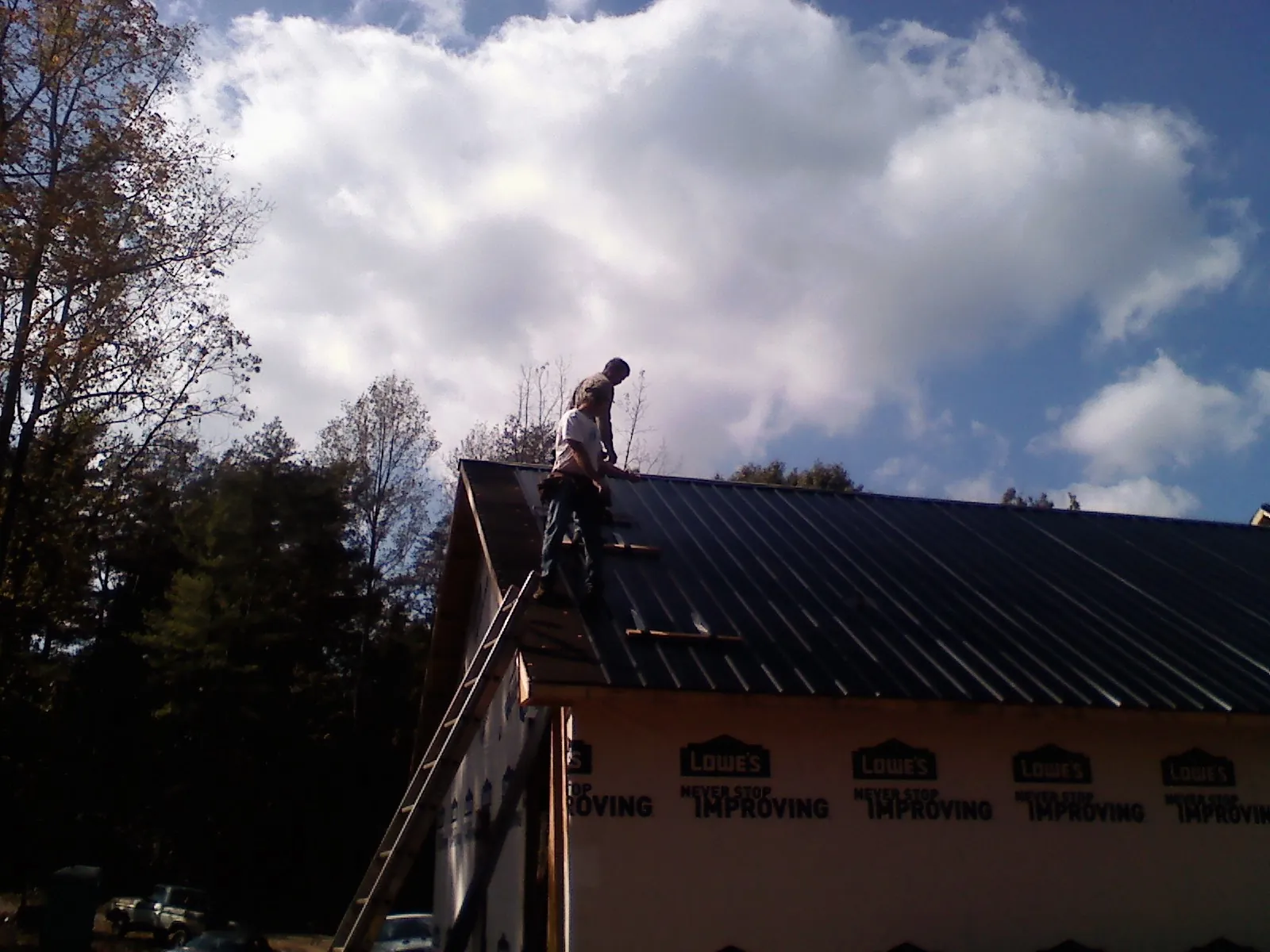 Roofer fastening dark metal panels high against a cloudy sky, from a Roof Inspection job in Island Heights