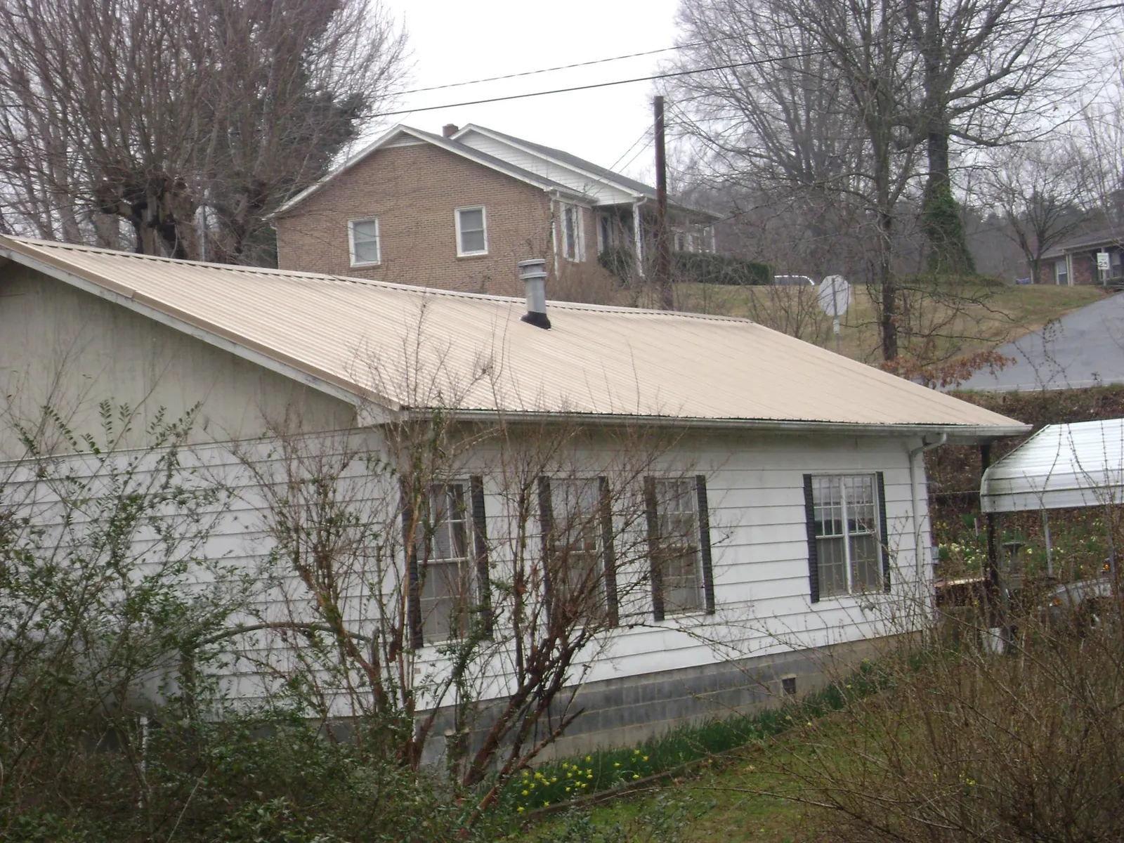 Tan metal roof on a white sided house set into a hillside — Commercial Roofing by Roofing Brothers in Island Heights